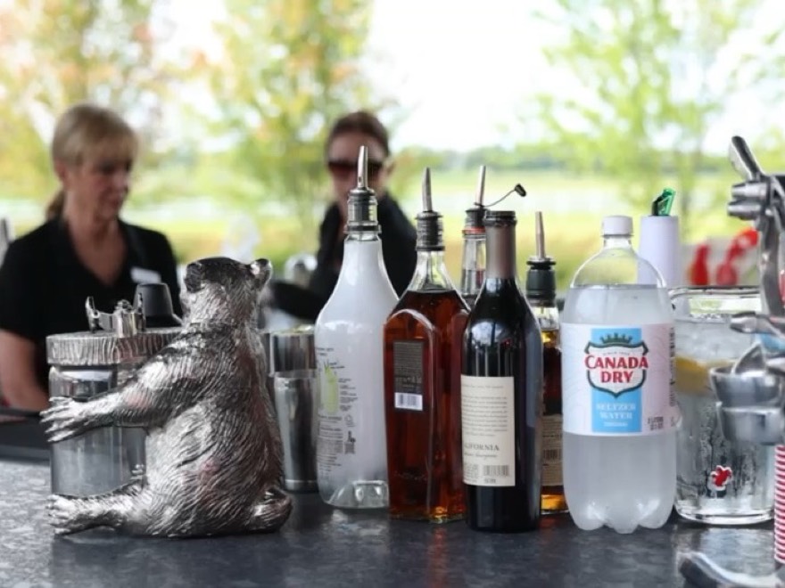 Two bartenders working behind an outdoor bar laid with spirits, mixers and glassware