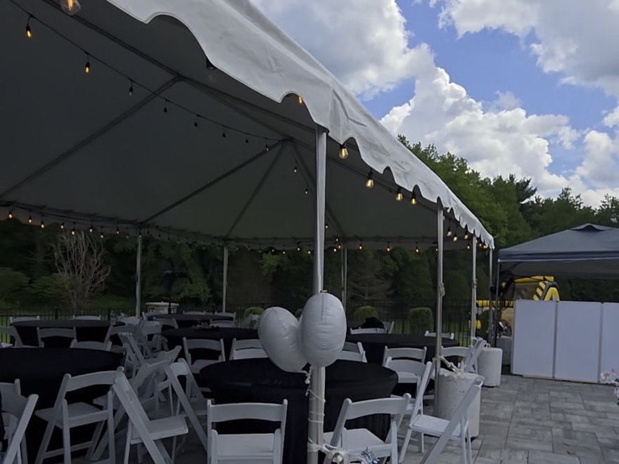 A white marquee hung with string lights over round tables in black linen and white folding chairs, set up on a paved terrace