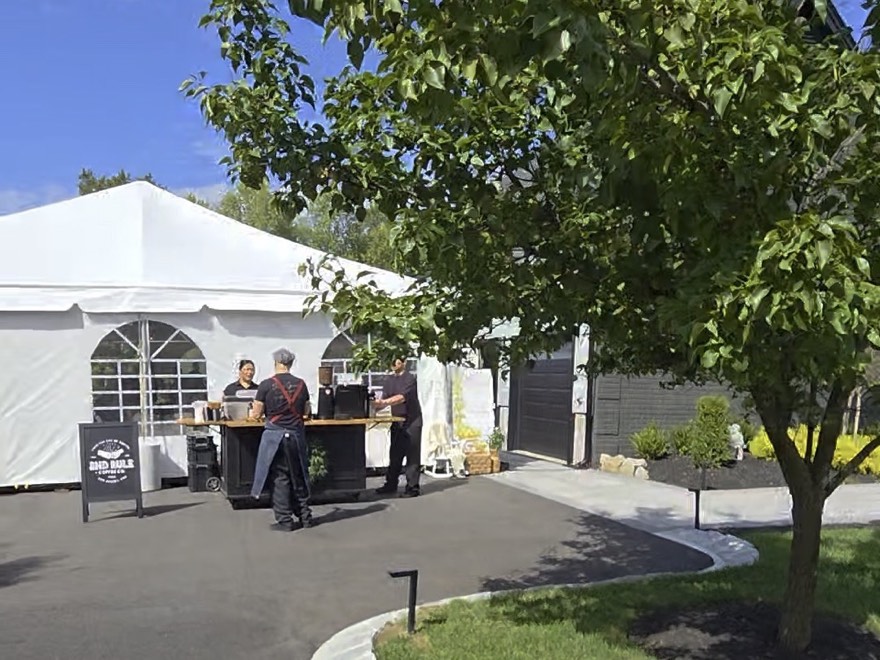 A white marquee erected on a residential driveway, with staff setting up a service counter beside it