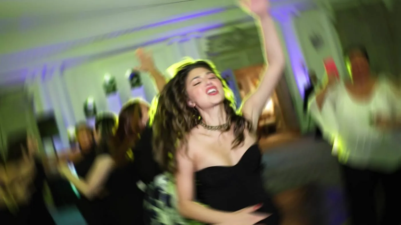Wedding guest dancing with her arms raised under green and purple uplighting on a packed dance floor