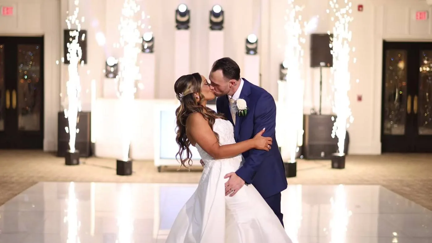 Newlyweds kissing alone on the dance floor as cold spark fountains fire behind them